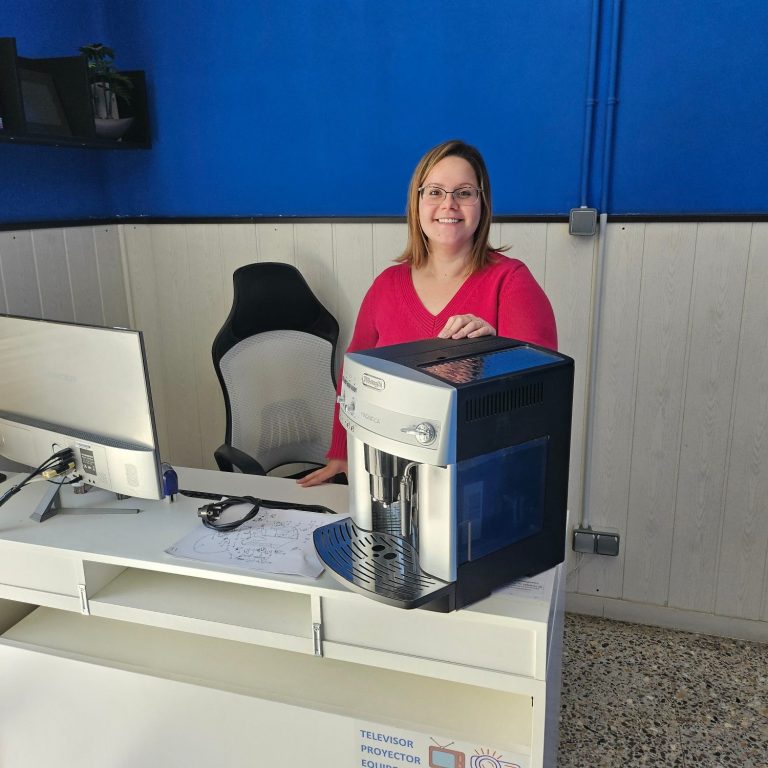 Mujer sonriente sentada frente a un escritorio con cafetera para reparar.